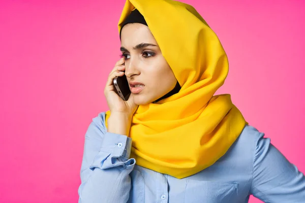 穿着黄色头巾的穆斯林妇女在电话粉色技术背景下交谈 — 图库照片