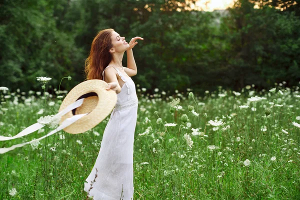 Donna in abito bianco e cappello in un campo con stile di vita fiori — Foto Stock