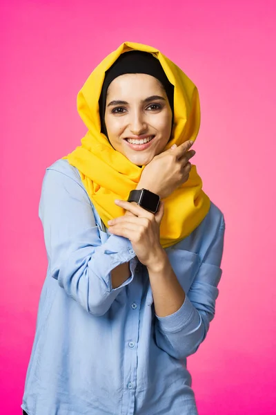 Femme gaie en jaune hijab technologie montre électronique utilisateur fond rose — Photo