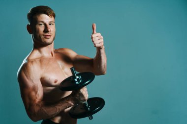 Elinde dambıllar olan atletik bir adam kas egzersizi yapıyor.