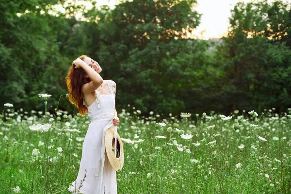 Donna in abito bianco e cappello in un campo con stile di vita fiori — Foto Stock