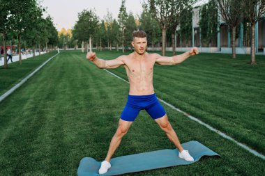 Mavi şortlu atletik adam parkta çalışıyor.