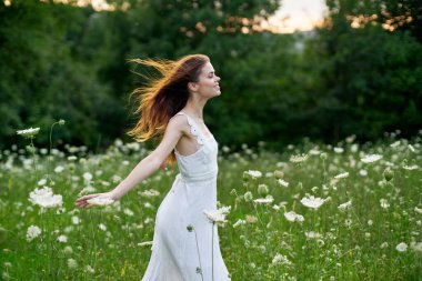 Çiçek tarlasında beyaz elbiseli bir kadın özgürce yürüyor.