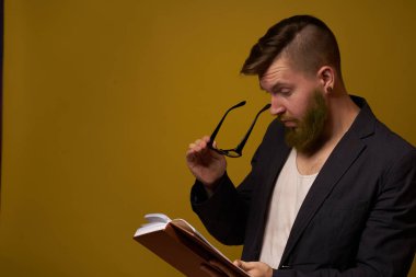 Siyah ceketli sakallı bir adam, elinde bir kitapla.