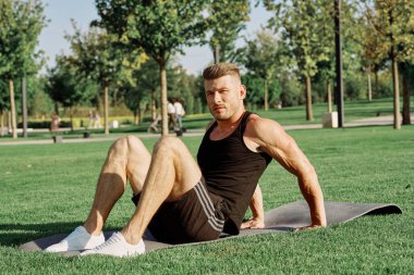 Sportif adam parkta çimlerde oturuyor.