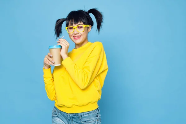 Vidám nő copfos sárga pulóverben ital kék háttér — Stock Fotó