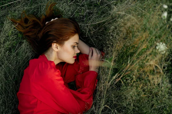 Hezká žena v červených šatech leží na trávě slunce letní příroda — Stock fotografie