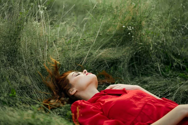 Pretty woman in red dress lies on the grass in the field nature fresh air — Stock Photo, Image