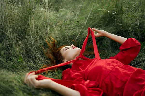 Hezká žena v červených šatech leží na trávě na poli příroda čerstvý vzduch — Stock fotografie