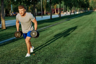 Dambılı erkek sporcu parkı CrossFit egzersizi yapıyor.