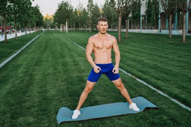 Mavi şortlu atletik adam parkta çalışıyor.