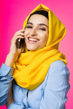 Sarı tesettürlü müslüman kadın telefon teknolojisi pembe arka planda konuşuyor.