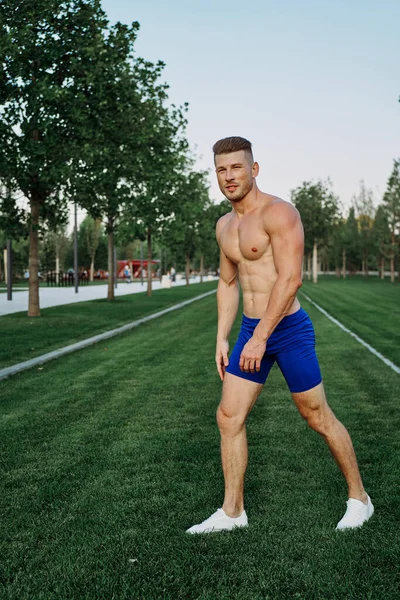 Athletic man with a pumped-up torso exercise in the park fitness — Stock Photo, Image