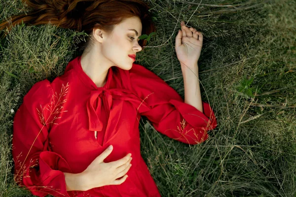 Pretty woman in red dress lies on the grass landscape freedom — Stock Photo, Image