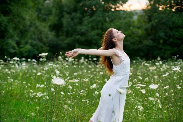 Femme gaie dans un champ avec des fleurs dans une robe blanche dans la nature — Photo