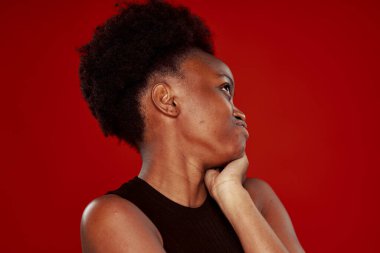 Siyah tişörtlü kıvırcık Afrikalı kadın. Kırmızı arka plan.
