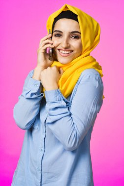 Sarı tesettürlü müslüman kadın telefonda pembe teknolojiyle konuşuyor.