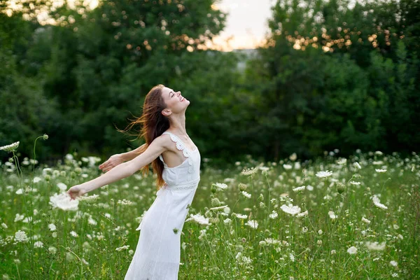 Весела жінка в полі з квітами в білій сукні на природі — стокове фото