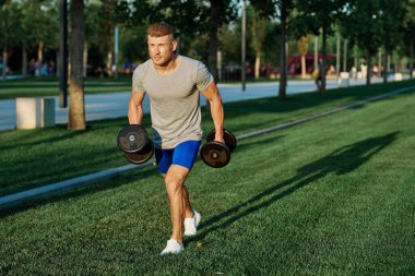 Dambılı erkek sporcu parkı CrossFit egzersizi yapıyor.