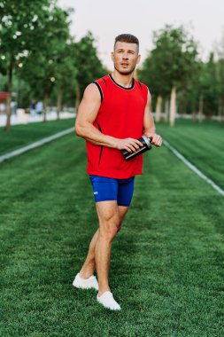 Kırmızı kolsuz tişörtlü atletik adam dışarıda spor yapıyor.