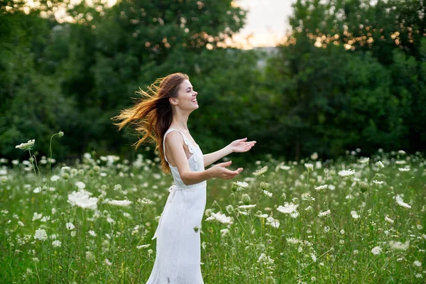 Χαρούμενη γυναίκα σε ένα πεδίο με λουλούδια σε ένα λευκό φόρεμα στη φύση — Φωτογραφία Αρχείου