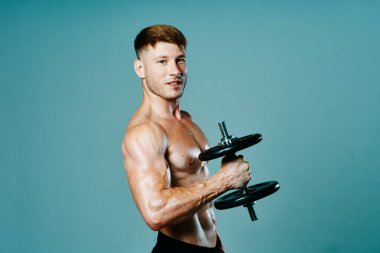 Vücudu kaslı, elinde dambıllar olan bir vücut geliştirici.