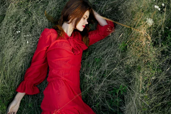 Hezká žena v červených šatech leží na trávě představovat horní pohled — Stock fotografie