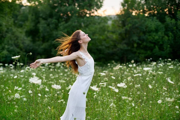 Glad kvinna på ett fält med blommor i en vit klänning i naturen — Stockfoto