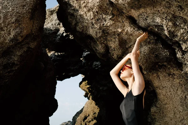 Nő fekete fürdőruhában pózol sziklák közelében óceán egzotikus — Stock Fotó