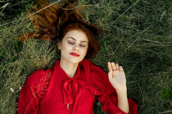 Vacker kvinna i röd klänning ligger på gräset landskap frihet — Stockfoto