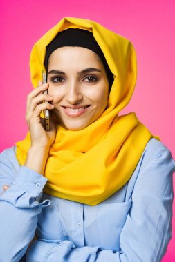 Sarı tesettürlü müslüman kadın telefon teknolojisi pembe arka planda konuşuyor.