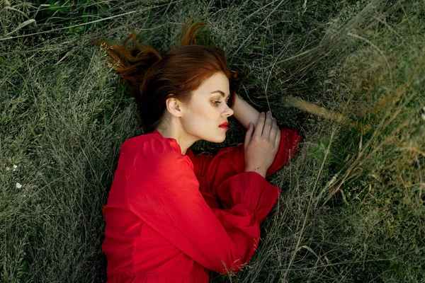Csinos nő piros ruhában fekszik a füvön nap nyár természet — Stock Fotó