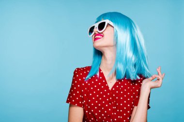 Mavi peruklu, güneş gözlüklü, neşeli bir kadın.