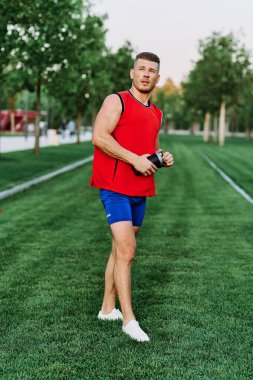 Kırmızı kolsuz tişörtlü atletik adam dışarıda spor yapıyor.
