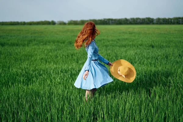 Kvinna i en blå klänning i ett fält i naturen hatt blommor gå — Stockfoto