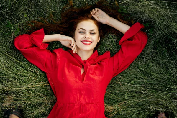 Kırmızı elbiseli neşeli kadın çimlerin üzerinde uzanıyor.