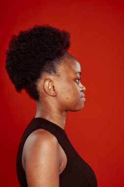 Siyah tişörtlü kıvırcık Afrikalı kadın. Kırmızı arka plan.