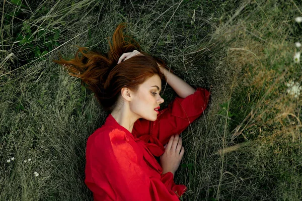 Vacker kvinna i röd klänning ligger på gräset sol sommar natur — Stockfoto