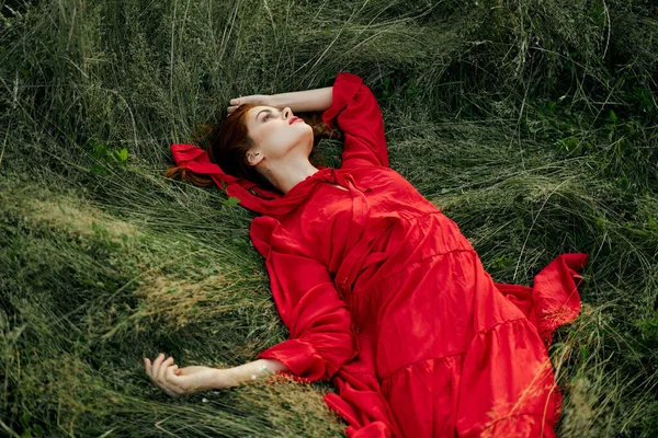 Γυναίκα με κόκκινο φόρεμα βρίσκεται στο γρασίδι στο τοπίο της φύσης τομέα — Φωτογραφία Αρχείου