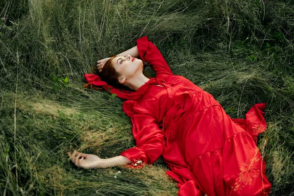 Γυναίκα με κόκκινο φόρεμα βρίσκεται στο γρασίδι στο τοπίο της φύσης τομέα — Φωτογραφία Αρχείου
