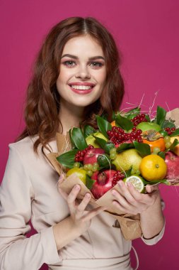 Güzel, parlak makyajlı, çekici bir kadın. Bir buket meyve, pembe arka plan.