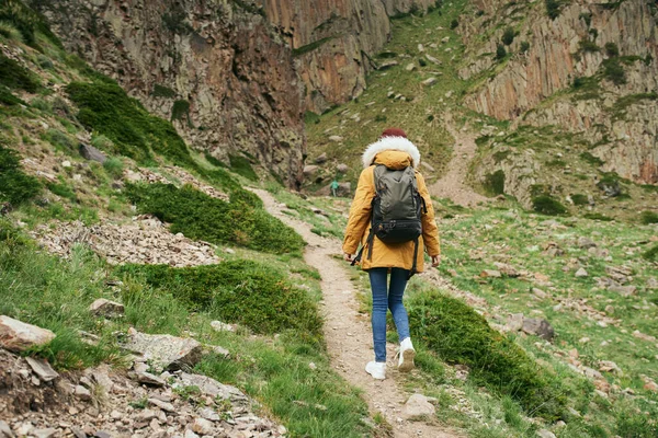 Mulher em uma jaqueta amarela com uma mochila nas montanhas viagem aventura — Fotografia de Stock