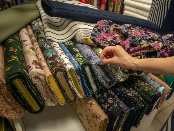 Tekstil salonundaki parlak doğal kumaşların geniş bir çeşitliliği. Bir kadının eli, yeni moda koleksiyonu için örneklerden kumaş seçer..