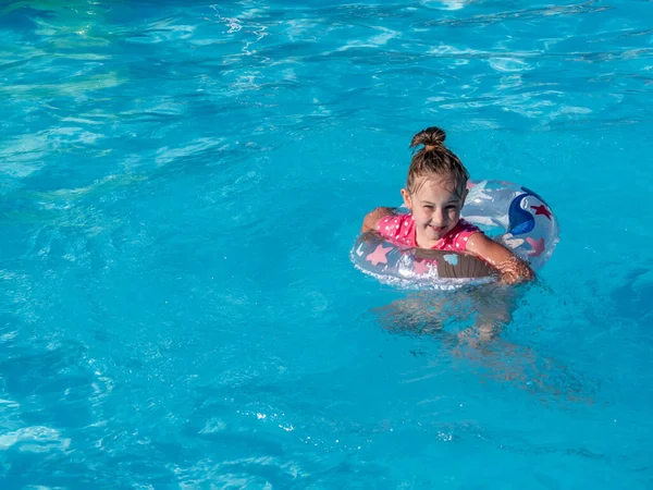 Lächelndes kleines Mädchen mit buntem aufblasbarem Ring im Pool mit blauem Wasser. — Stockfoto