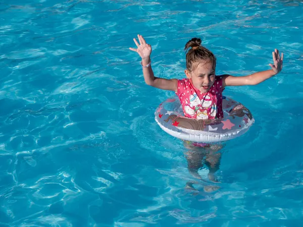 Lächelndes kleines Mädchen mit buntem aufblasbarem Ring im Pool mit blauem Wasser. — Stockfoto