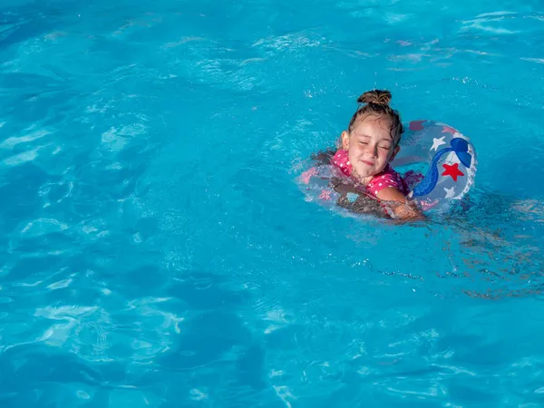 Kleines Mädchen mit buntem aufblasbarem Ring im Pool mit blauem, klarem Wasser. — Stockfoto