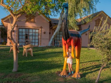 Küçük kız güneşli bir günde parkta büyük kahverengi bir dinozorun yanında..