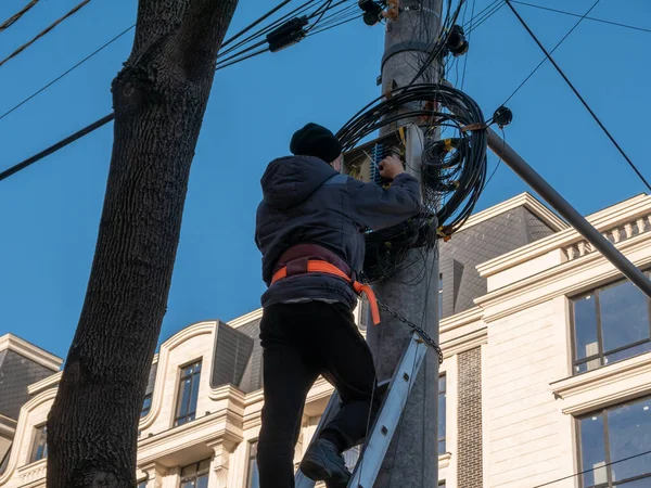 Un electricista en una escalera instala una caja de conexiones para Internet en un poste. — Foto de Stock