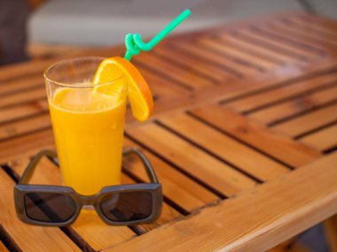 Masanın üzerinde bir bardak portakal suyu ve güneş gözlüğü var..
