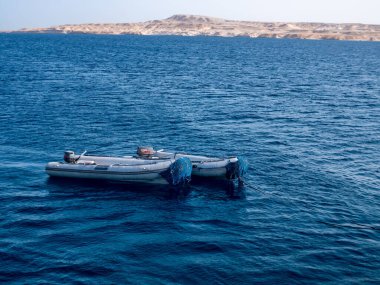 Mavi denizin ve adanın arka planında iki lastik motorlu tekne..
